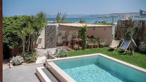 A swimming pool with a view of the sea, surrounded by greenery and a small patio area.