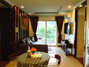 Relax in this stylish living room with a comfortable sofa, dining table for two, and a large window with curtains.