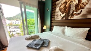 A hotel room with a large bed, two towels, a lamp, and a painting of an elephant on the wall.
