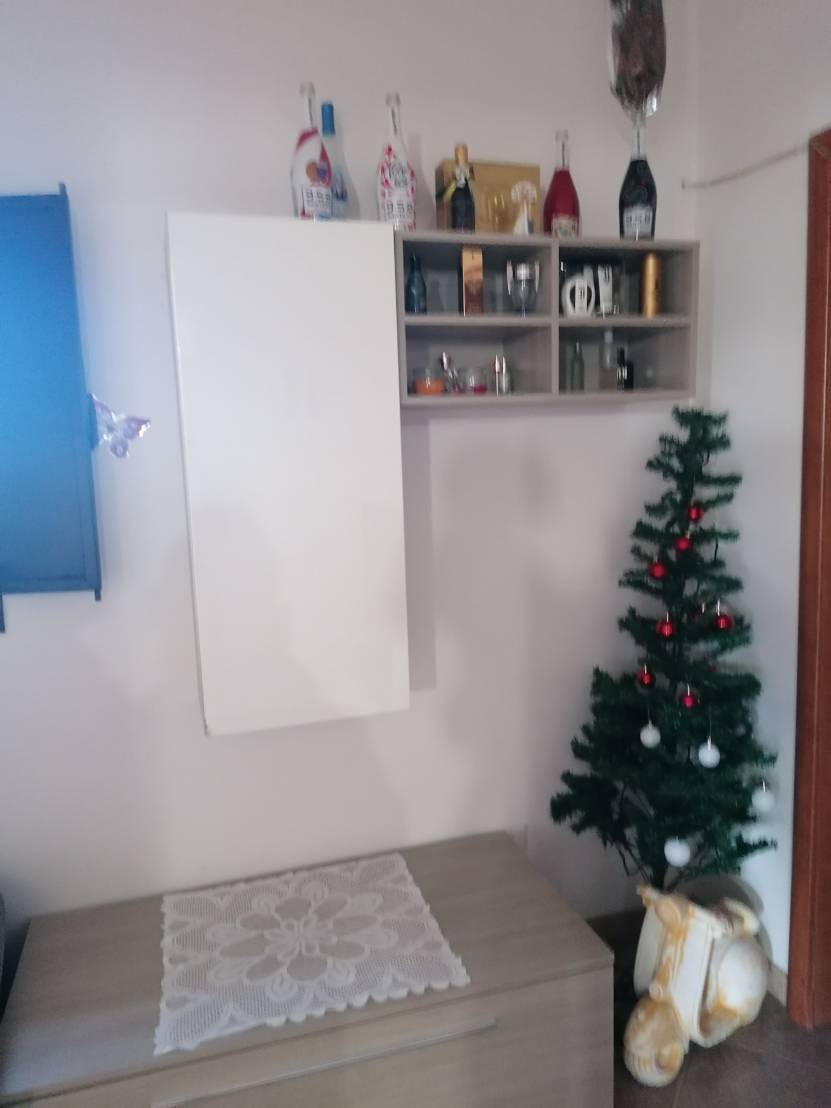 A room with a whiteboard, a small Christmas tree, and a shelf with various items.
