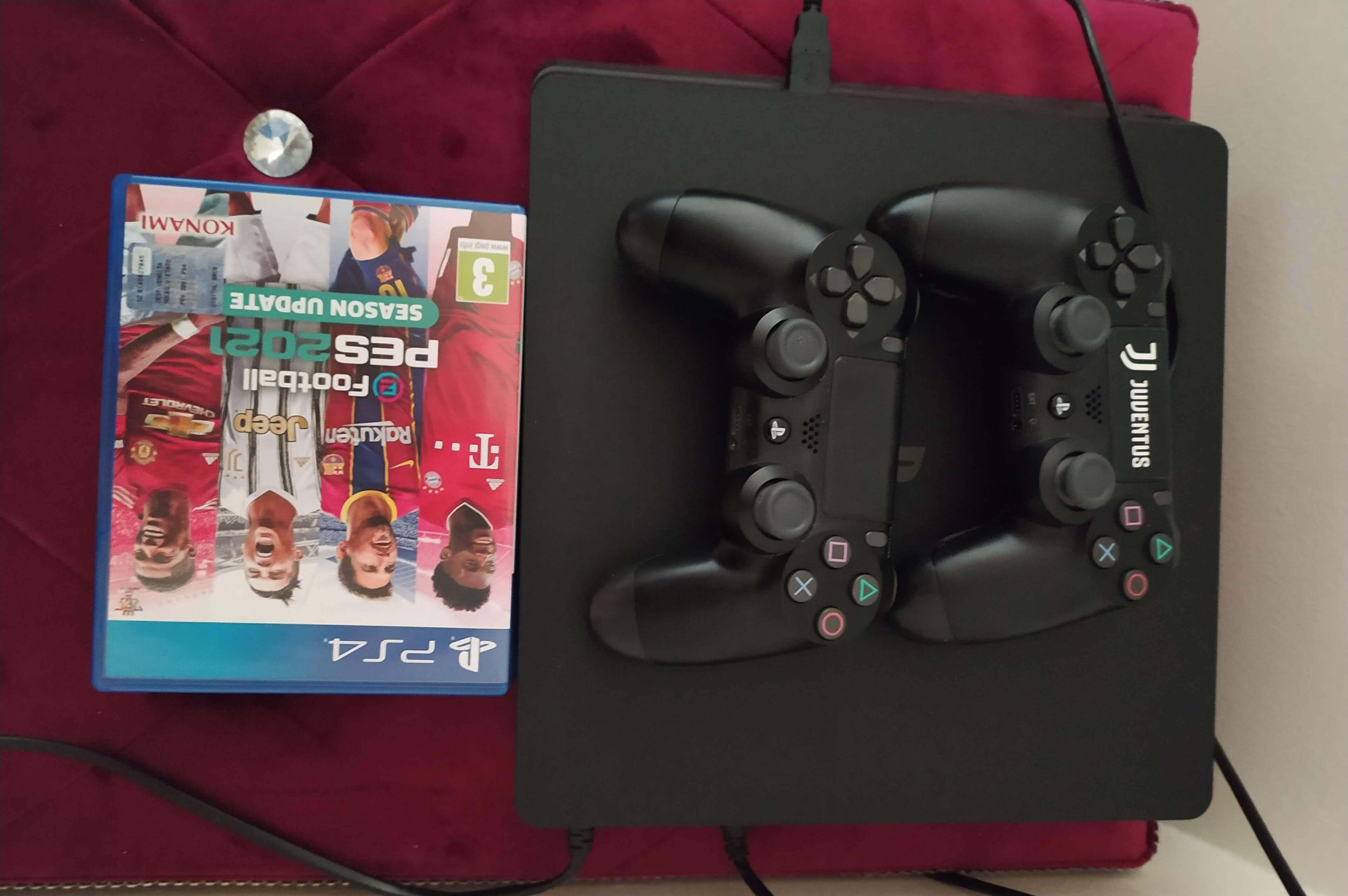 Een gamingopstelling met een PlayStation 4 controller en een speldoosje op een rode ondergrond.
