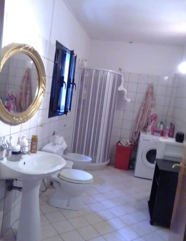 A bathroom with a sink, two toilets, a shower, and a washing machine. - Independent Apartment From Vincenza (Lentini)