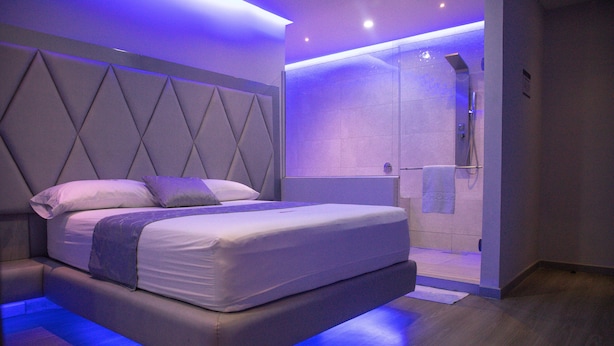 A modern bedroom with a large bed, a built-in headboard, and a shower area. - Hotel ByHours Circunvalar (Barranquilla)
