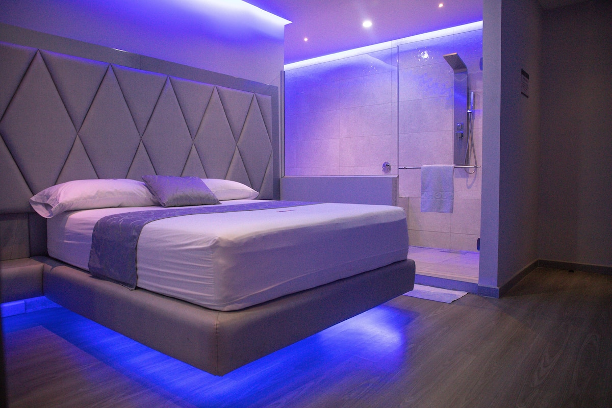 A modern bedroom with a large bed, a built-in headboard, and a shower area.