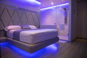 Un dormitorio moderno con una cama grande, cabecera integrada y zona de ducha.