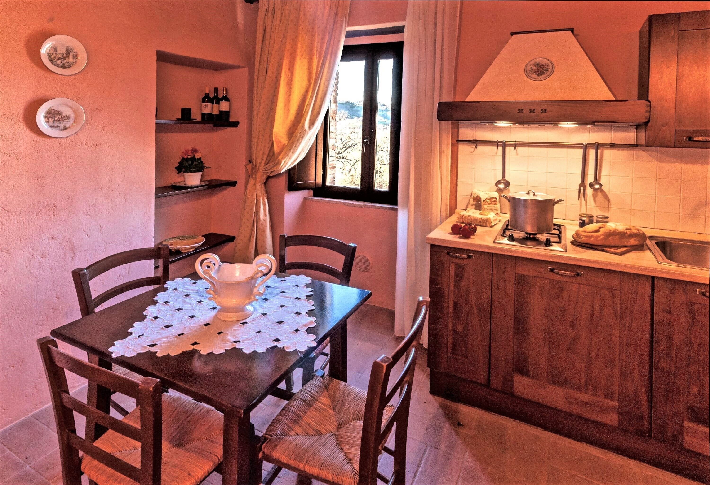 Una cocina acogedora con armarios de madera, una mesa de comedor con mantel de encaje y una ventana con cortinas.