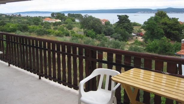A balcony with a view of a lake, a wooden table, and a white plastic chair. - Nar Apartment A4 - With sea View Terrace (Pasman)