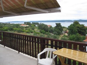 Un balcon donnant sur un lac, une table en bois et une chaise en plastique blanche.