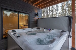 A hot tub with a control panel, a window, and a view of trees. - Luxurious cabin with outdoor pool access, paved roads, oversized garage (Lead)