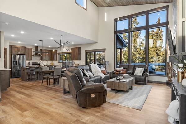 A spacious living area with a large window, a kitchen with wooden cabinets, and a comfortable seating area with a sofa and chairs. - Luxurious cabin with outdoor pool access, paved roads, oversized garage (Lead)