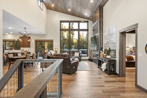 A spacious living area with a high ceiling, large windows, and a modern kitchen.