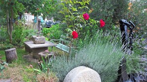 Ein Garten mit einer Steinsitzbank, einem Steinpflanzkübel mit Grünpflanzen und einer Statue.