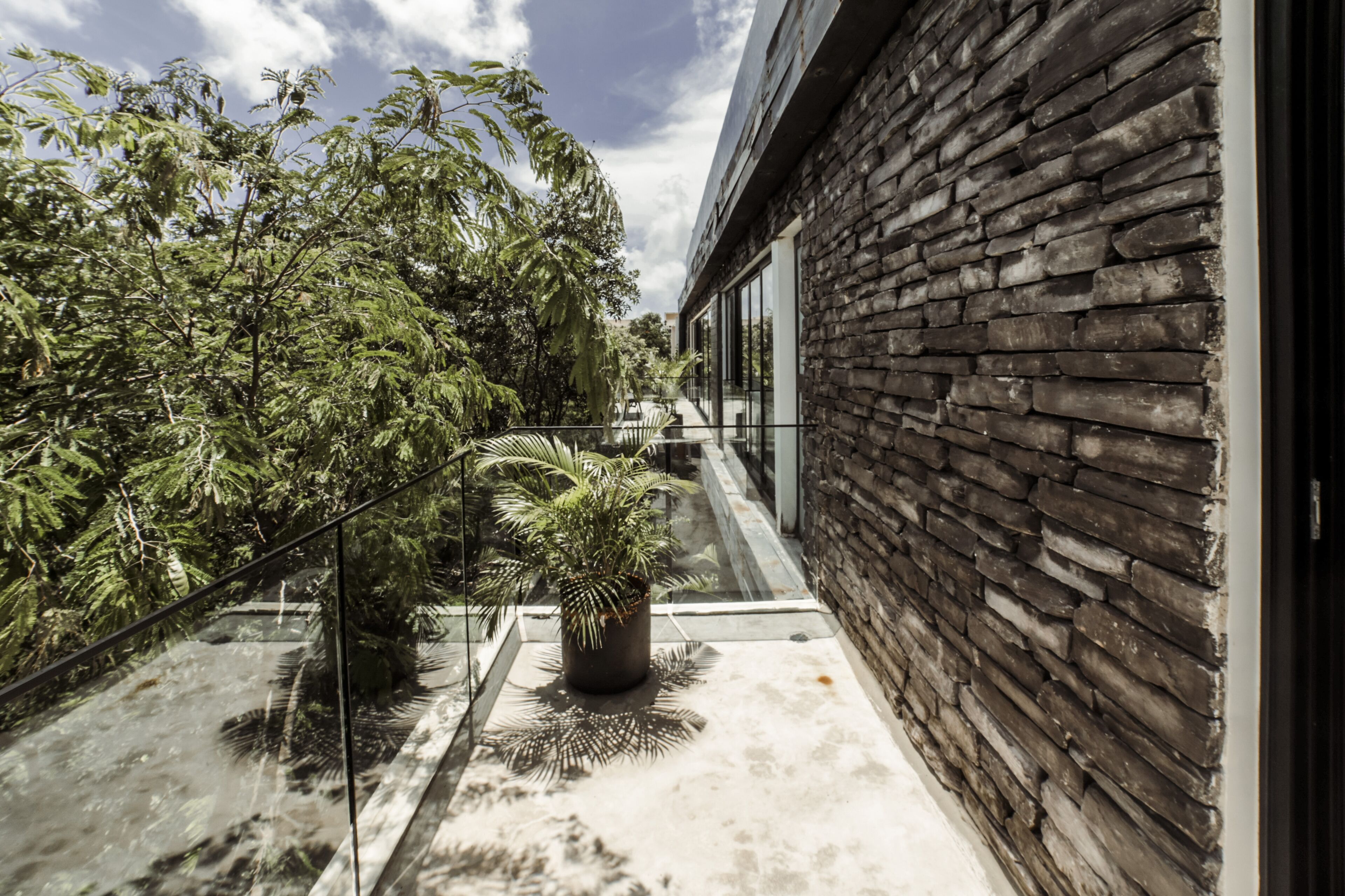 A modern building with a stone facade and a glass balcony overlooking lush greenery.