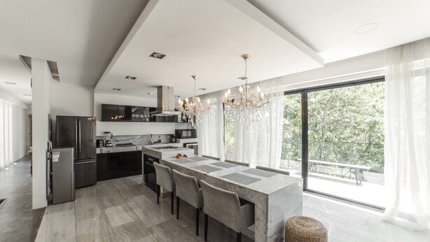 Een moderne keuken met een centraal eiland, roestvrijstalen apparatuur en een groot raam met uitzicht op groen.
