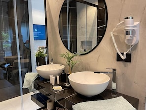 Une salle de bain moderne avec deux grands lavabos blancs, un miroir rond, un sèche-cheveux et un porte-serviettes.