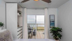 Un dormitorio con una cama grande, un ventilador de techo, vista a un balcón con mobiliario exterior y una planta en maceta.