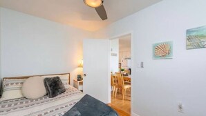 Un dormitorio con cama, una mesita de noche, una lámpara y una puerta que da a un comedor.
