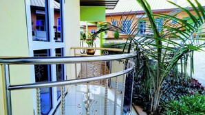 Balcó de vidre corbat amb barana metàl·lica, envoltat de plantes en testos i vista d'un edifici amb un rètol.