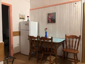 A compact kitchen with a white refrigerator, wooden chairs, a table with a checkered tablecloth, and a vase with a red flower. - Nar Apartment A3 - With sea View Balcony (Pasman)