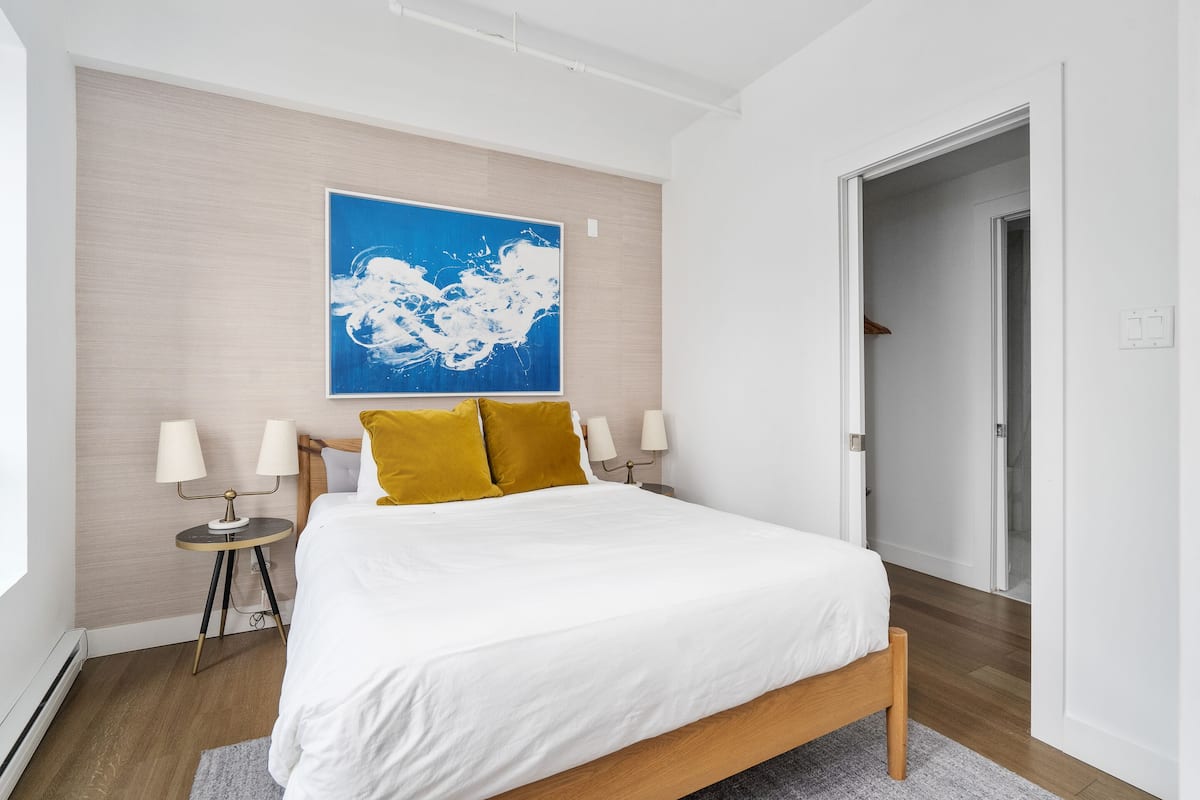 Una habitación de hotel moderna con una cama grande, un cuadro abstracto azul en la pared y suelo de madera.