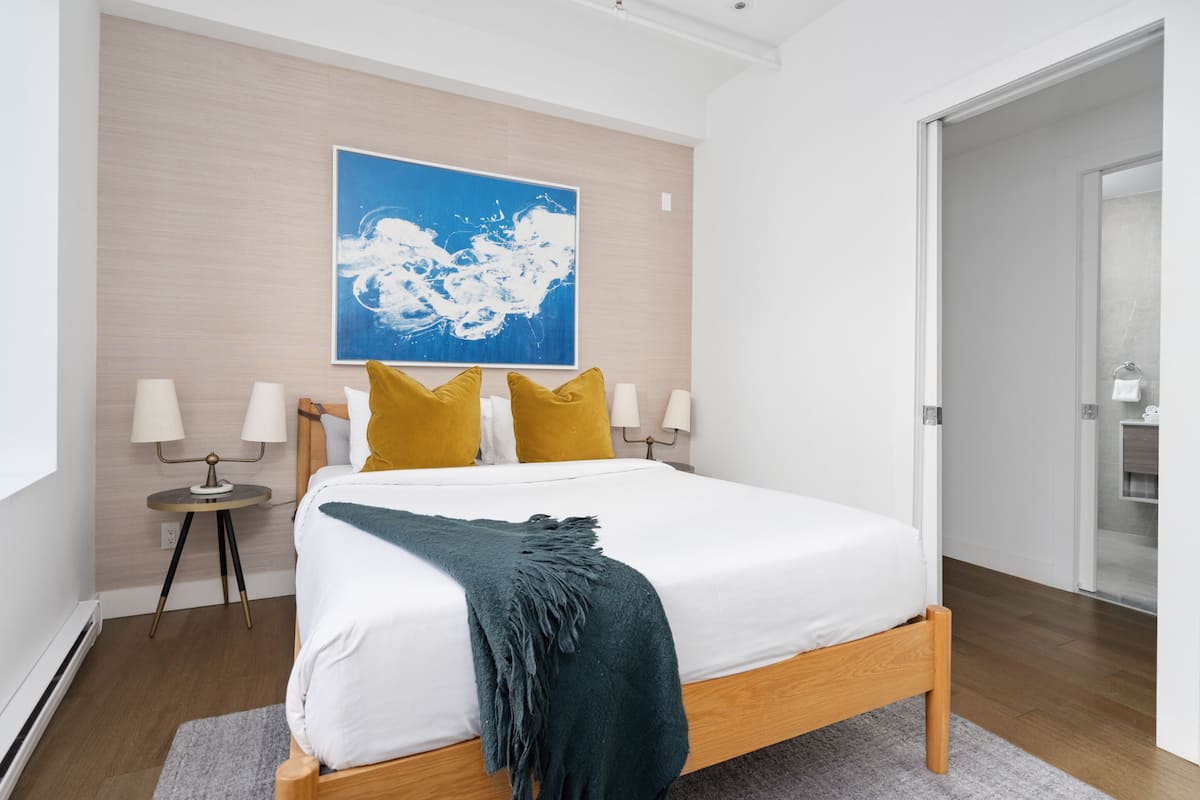 Un dormitorio moderno con una cama de madera, un cuadro abstracto azul y una mesita de noche con lámparas.