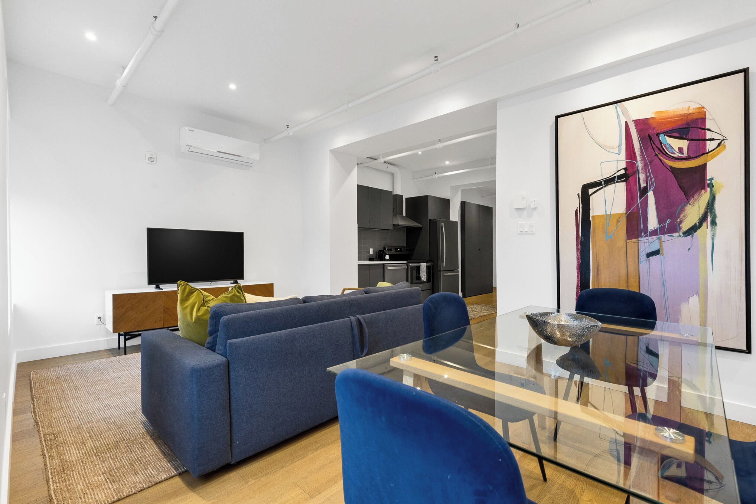 A modern living room with a sofa, a glass dining table, and a flat-screen TV.