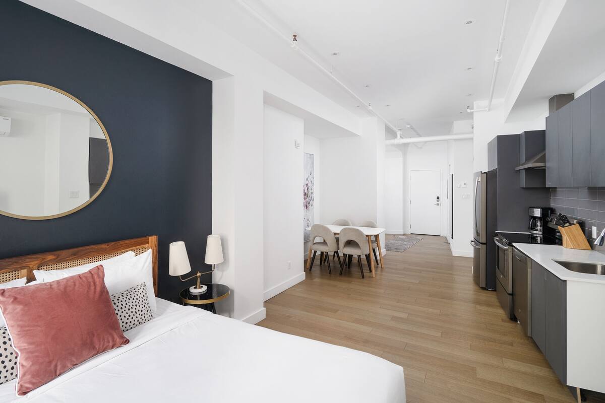 Una habitación de hotel moderna con cama, mesita de noche, lámpara y vistas al comedor.
