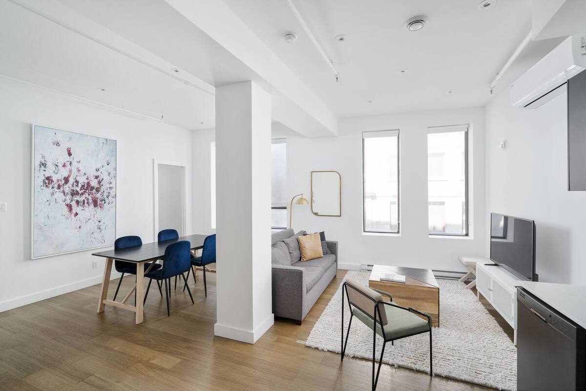Una sala de estar moderna con comedor, un sofá gris, un televisor y obras de arte en la pared.