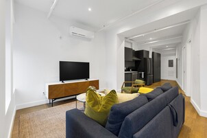 Ett modernt vardagsrum med en platt-TV, en soffa och en matplats, med ett kök synligt i bakgrunden.