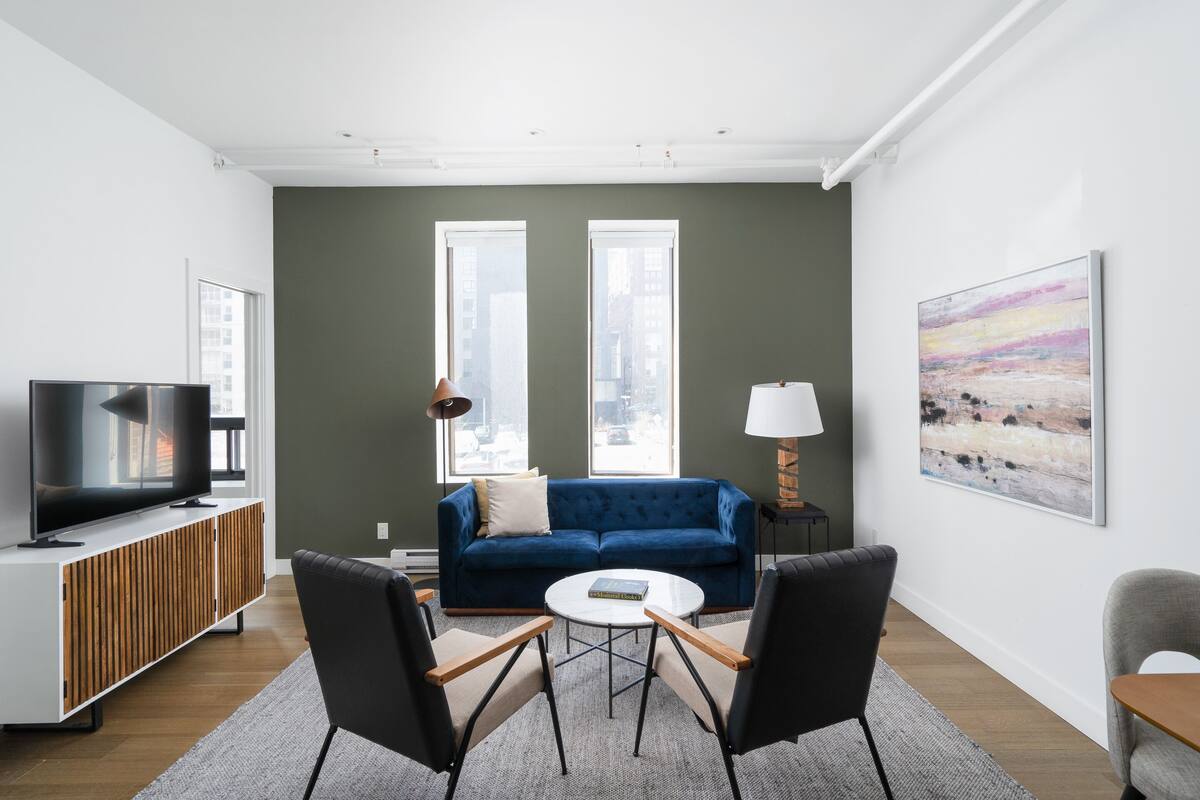 Una sala de estar moderna con un sofá azul, un televisor sobre un mueble de madera, una mesa de centro redonda y dos sillones.