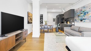 Una sala de estar moderna con un televisor de pantalla plana, un sofá gris y un comedor con una mesa y sillas.