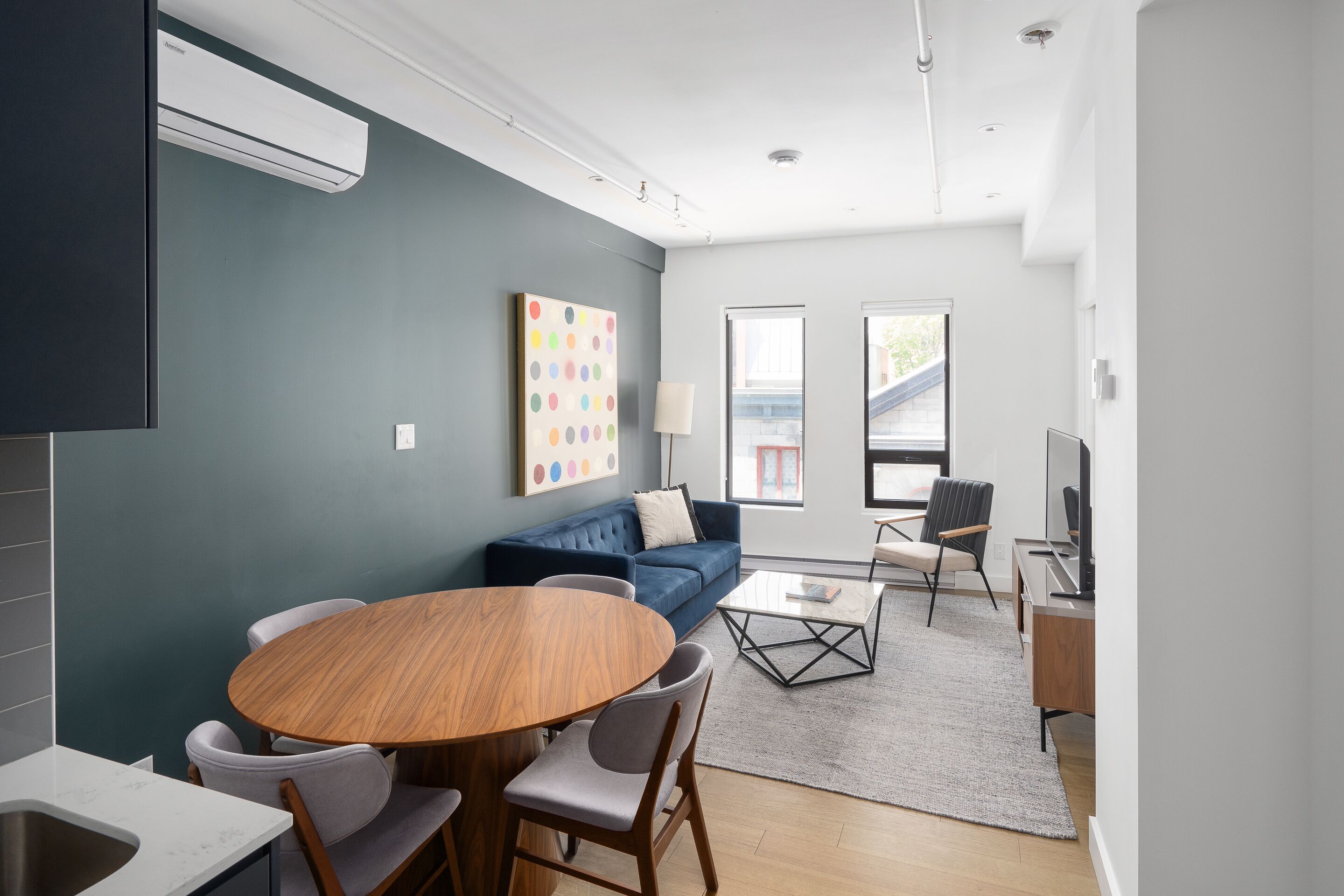 Una sala de estar moderna con un sofá azul, una mesa de comedor redonda de madera y una mesa de centro.