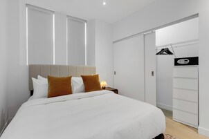 A modern hotel room with a large bed, a bedside table with a lamp, a wardrobe, and a walk-in closet.