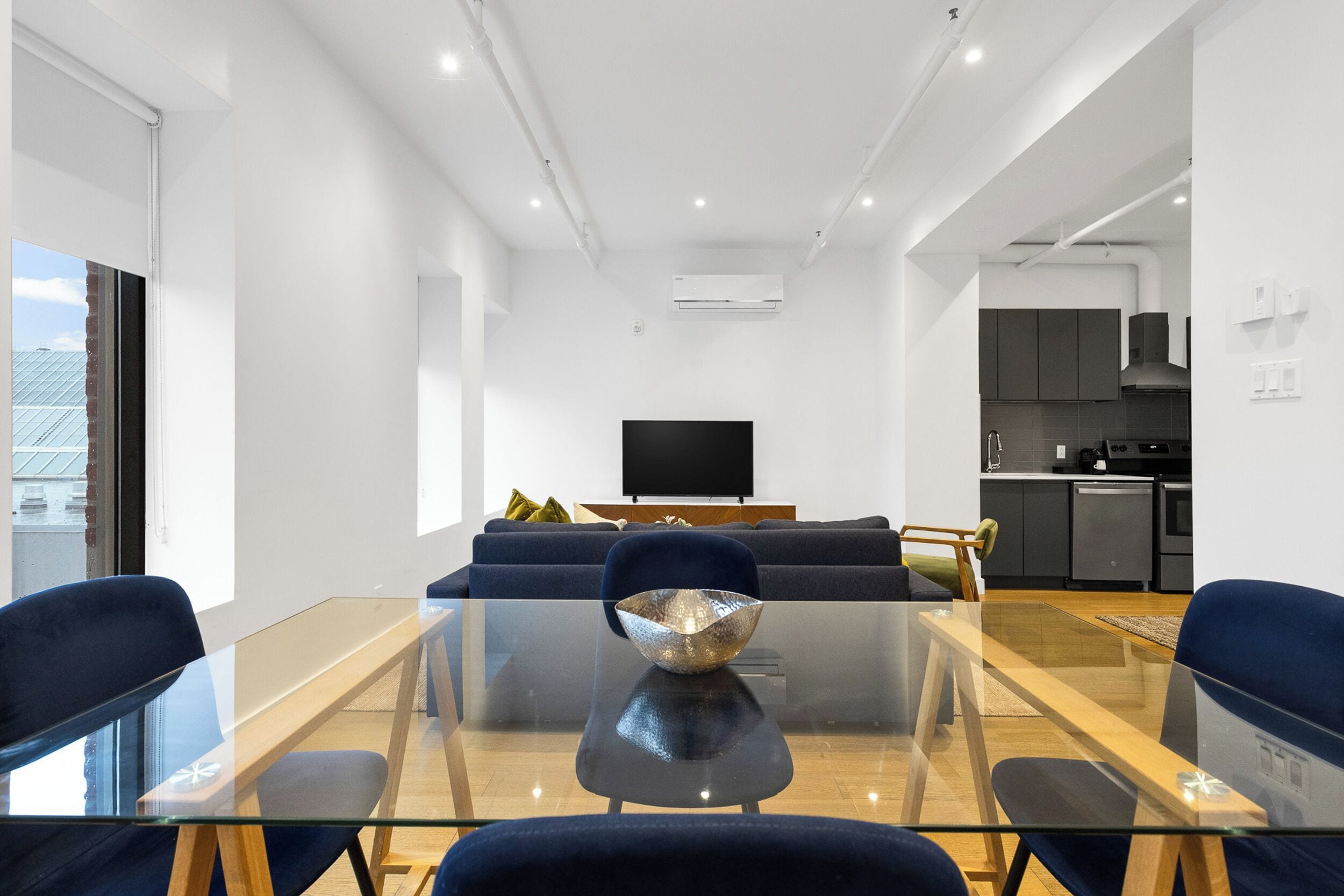 A modern living room with a glass coffee table, dark blue sofas, and a flat-screen TV.