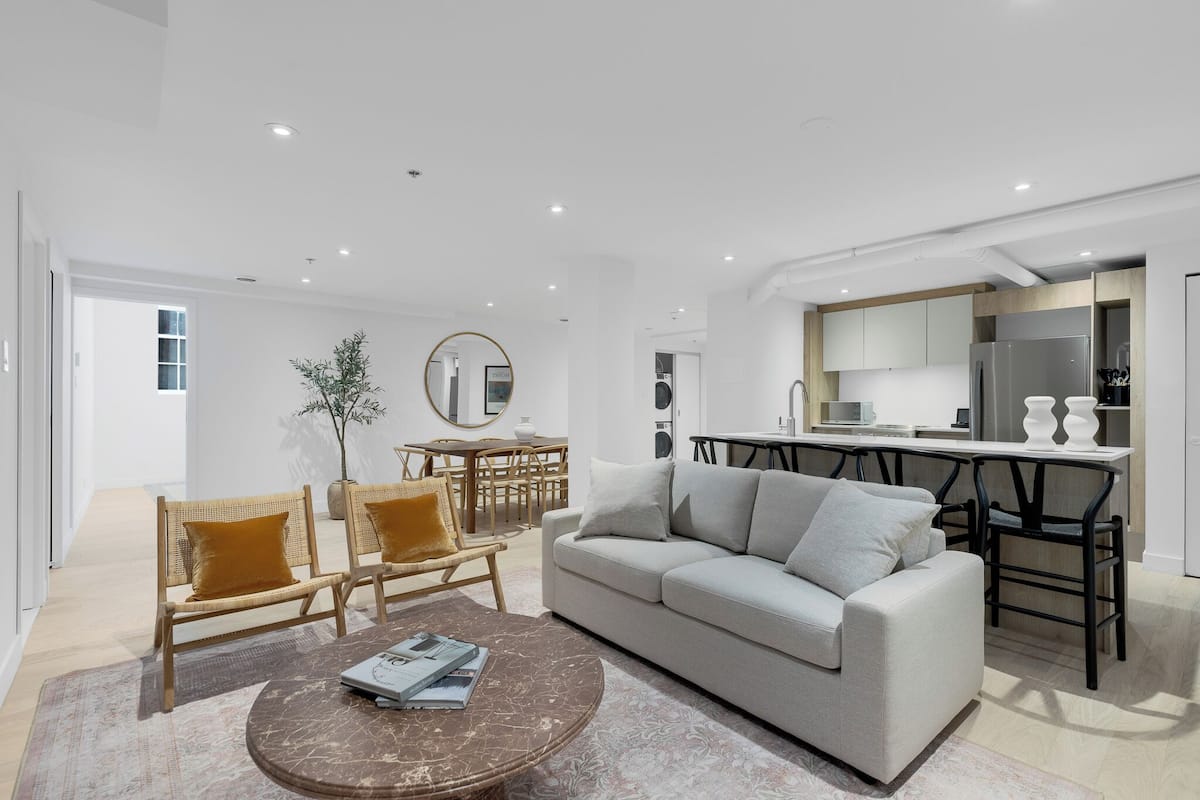 Una sala de estar moderna con un sofá, dos sillones, una mesa de centro y una zona de comedor con una mesa y sillas.
