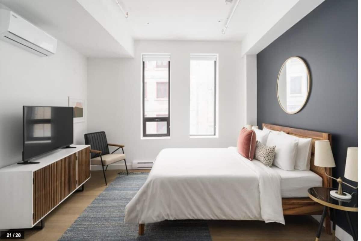 Una habitación de hotel moderna con cama, televisión, zona de estar y un ventanal grande.