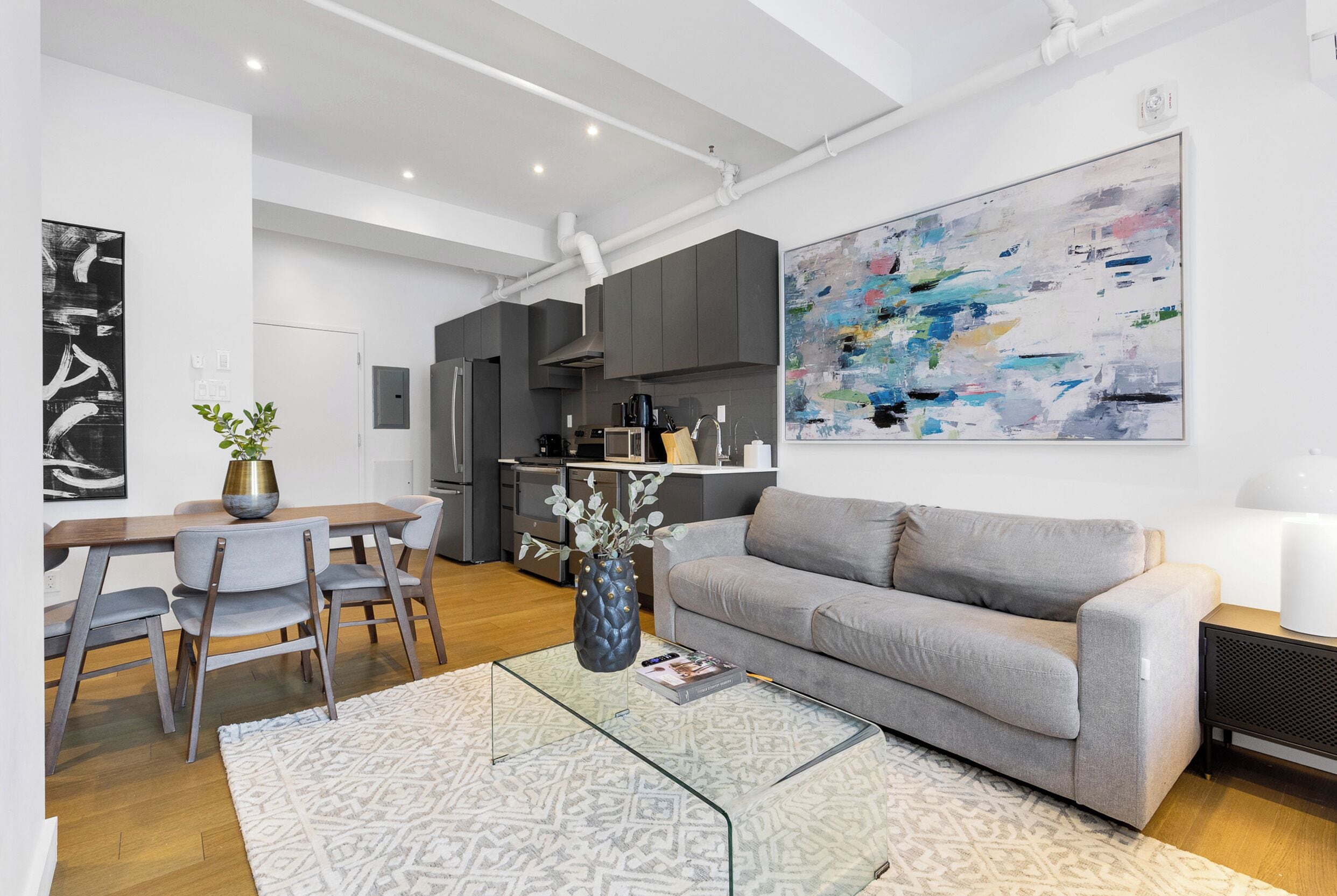 A modern living room with a grey sofa, a glass coffee table, and a dining area with a wooden table and chairs.