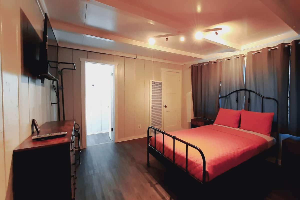 A bedroom with a bed, a desk, a TV, and a window with curtains.