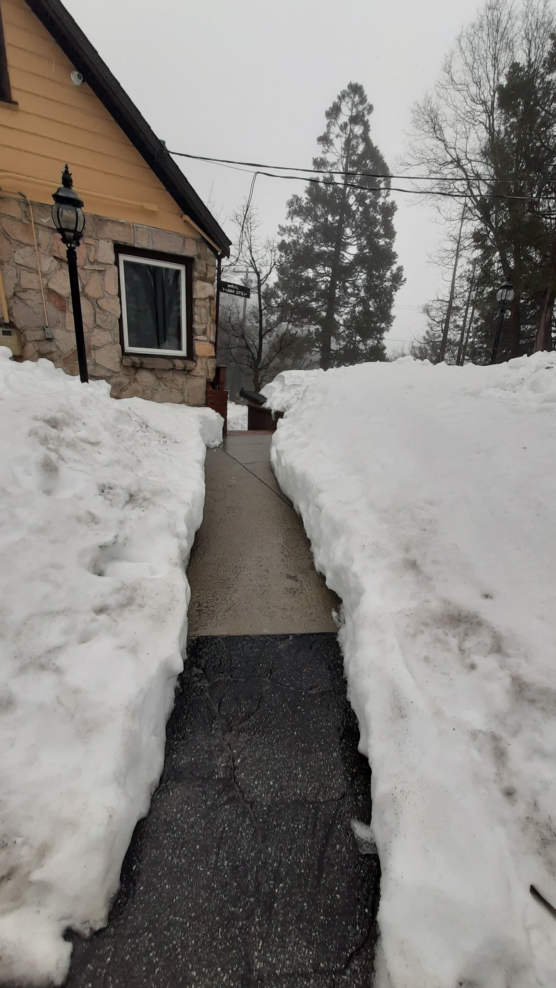 Uma trilha coberta de neve que leva a uma casa com fachada de pedra e uma janela.