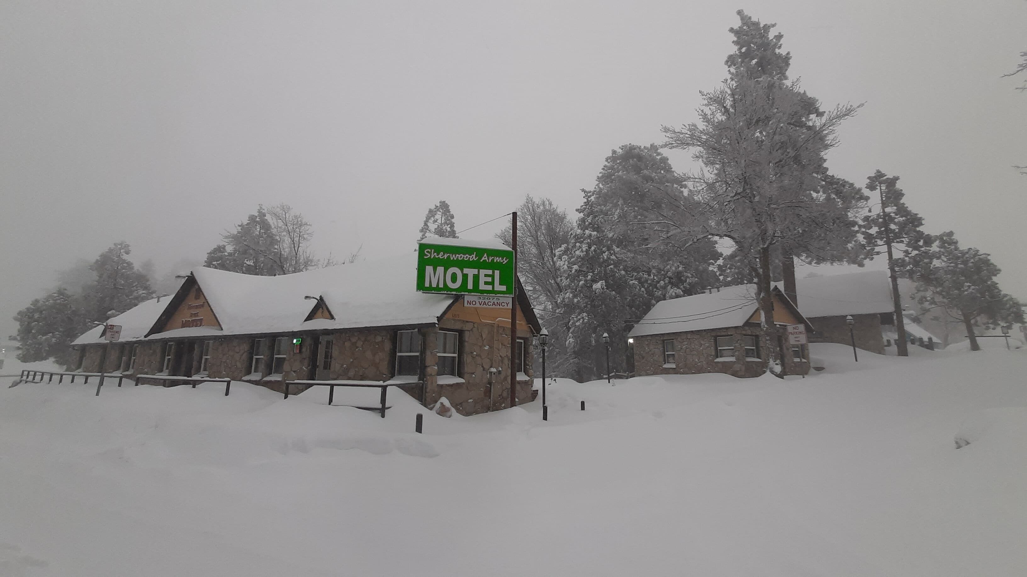 A motel with a stone facade, a green signboard, and snow-covered surroundings.