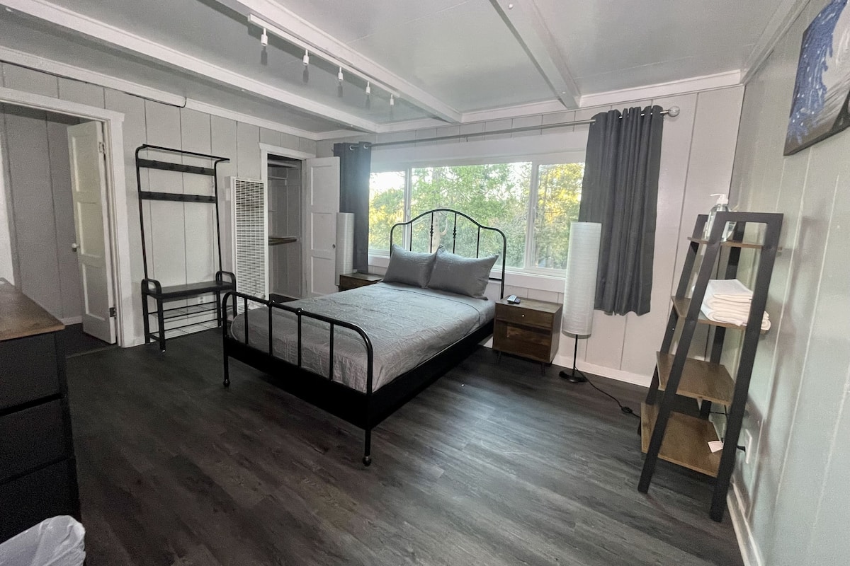 A bedroom with a bed, a bedside table, a lamp, a wardrobe, and a window with curtains.