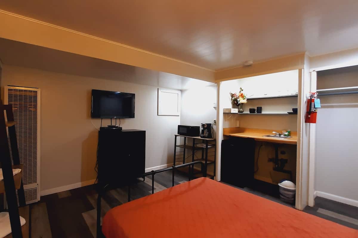 A hotel room with a bed, a desk with a computer, a TV, and a kitchenette.