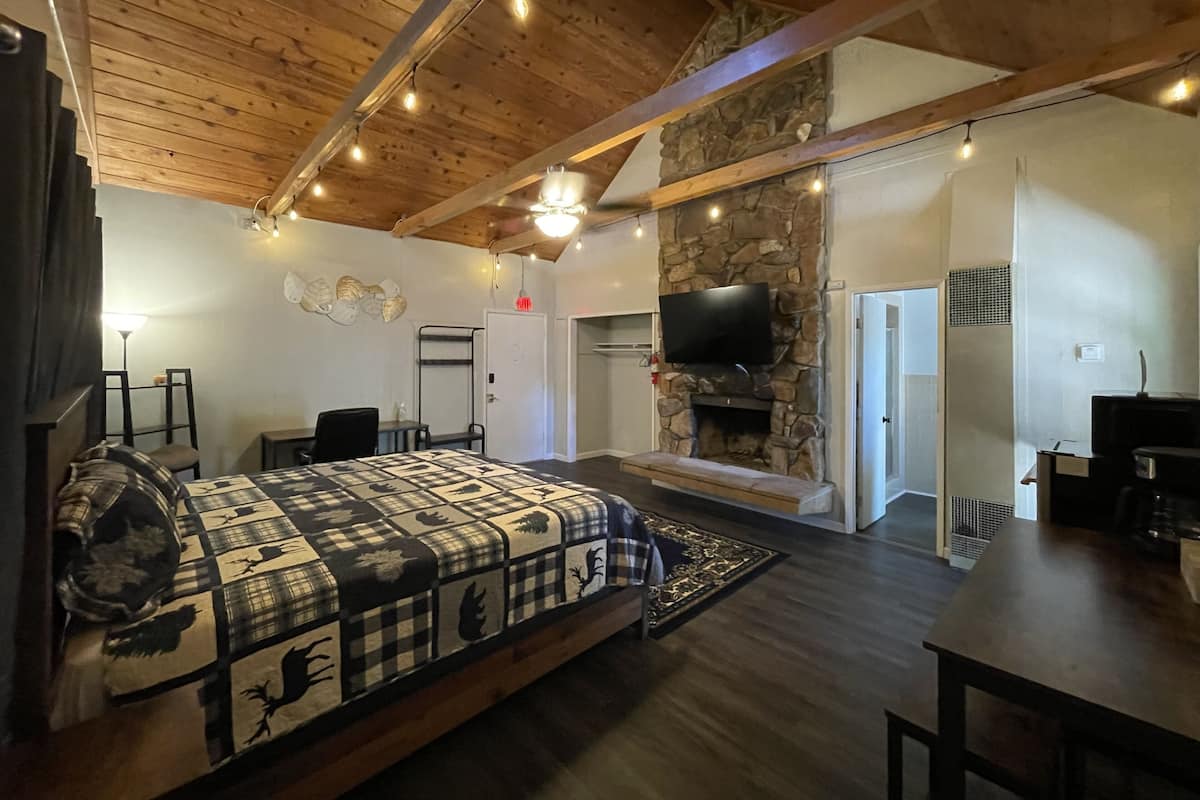 A spacious bedroom with a large bed, a stone fireplace, and a television mounted on the wall.