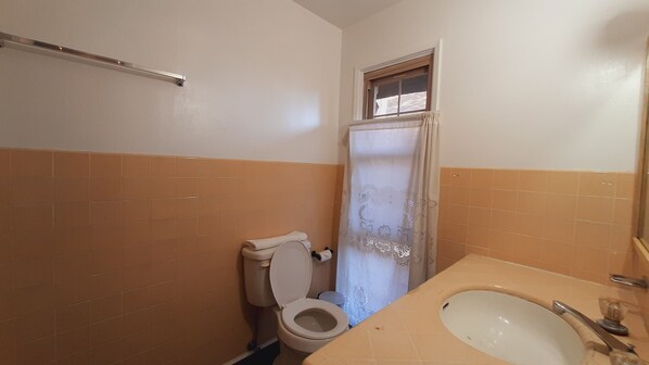 Un baño con inodoro, lavabo y ventana sobre el inodoro.