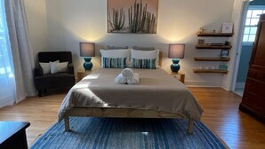 Une chambre à coucher comprenant un lit, deux lampes de chevet, une chaise, une étagère fixée au mur et une porte.