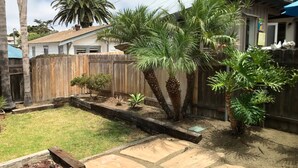 Un jardin avec une clôture en bois, des palmiers et une terrasse en pierre.