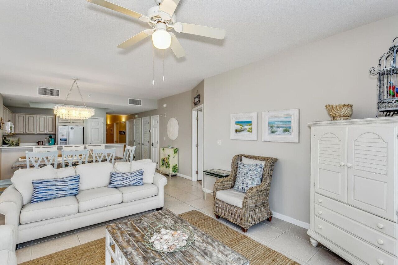 A living room with a white sofa, a wicker chair, a coffee table, and a white cabinet.