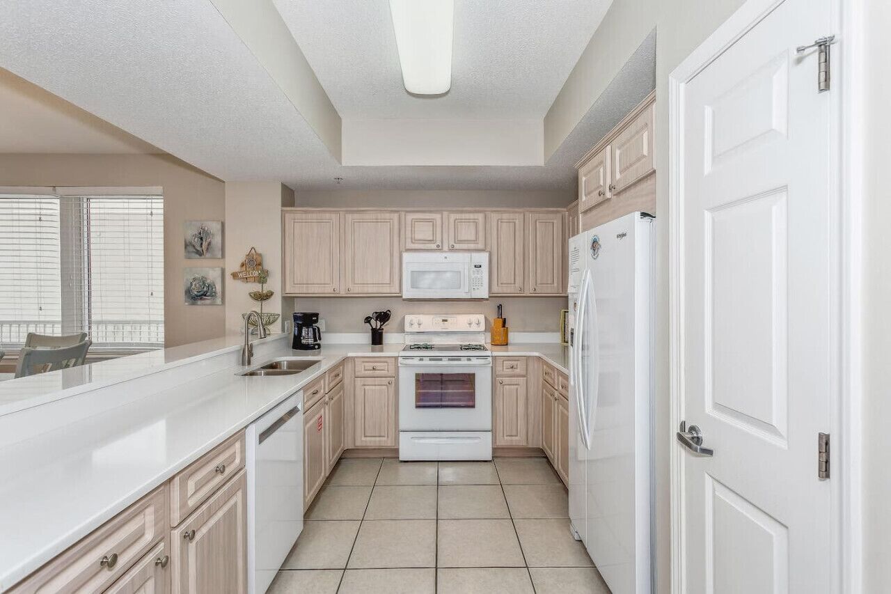 A kitchen with light wood cabinets, a white stove, a microwave, and a refrigerator.