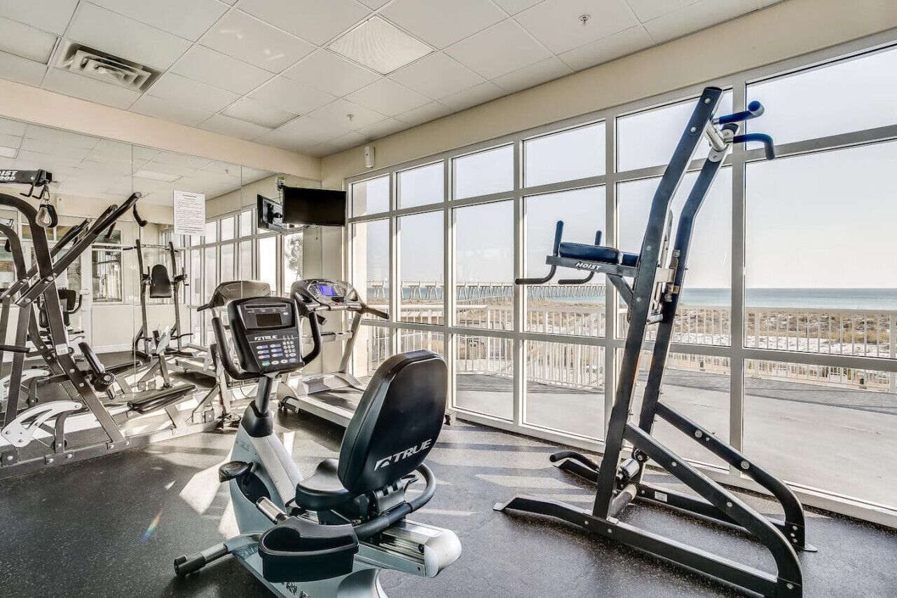 A gym with cardio machines, weight equipment, and large windows offering a view of the city.