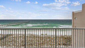 A beach view with a pier extending into the ocean, a sandy beach, and a building with a balcony. - Serenity Now: 9th Floor Summerwind West Condo Located Directly on the Gulf! (Navarre)